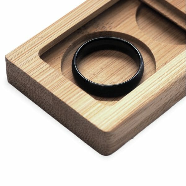 Black wedding ring in a wooden ring box on white background.