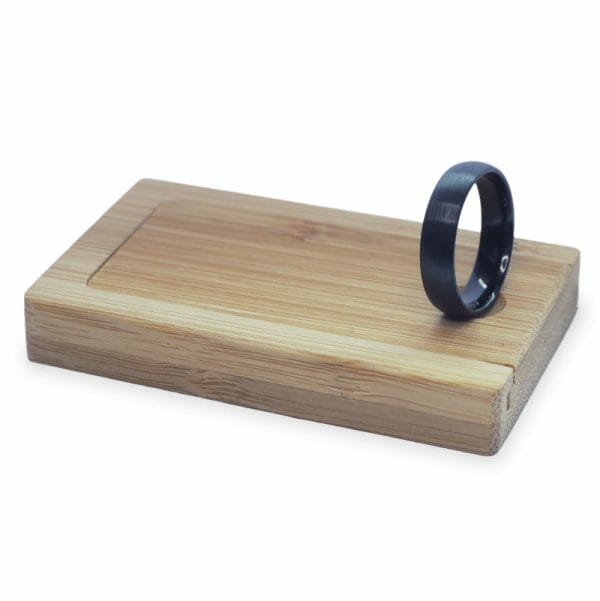 Black wedding ring in a wooden ring box on white background.